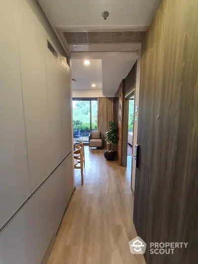 Modern apartment hallway leading to a bright living room with large windows and greenery view.