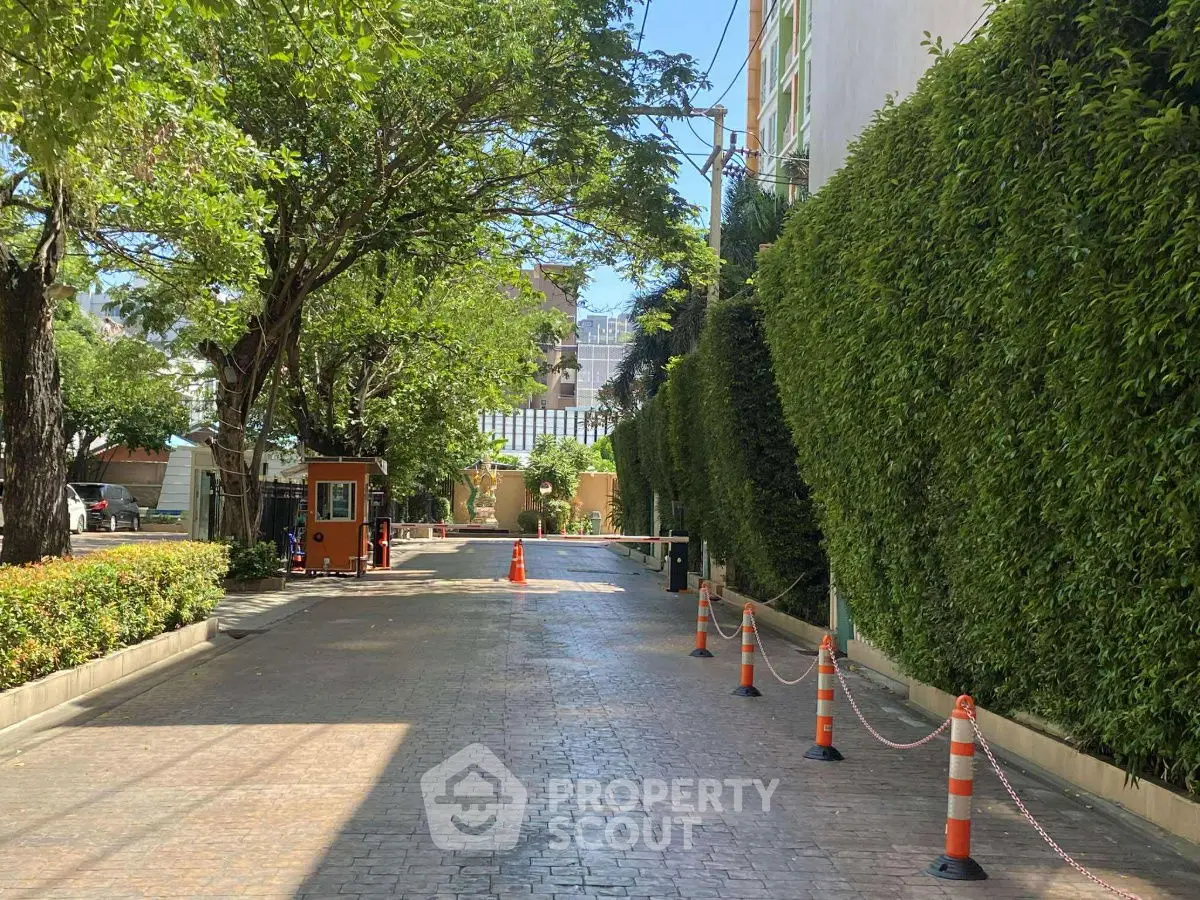Charming garden entrance with lush greenery and secure gated access in a residential complex.