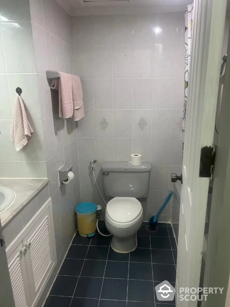 Compact bathroom with tiled walls and floor, featuring a toilet and sink.