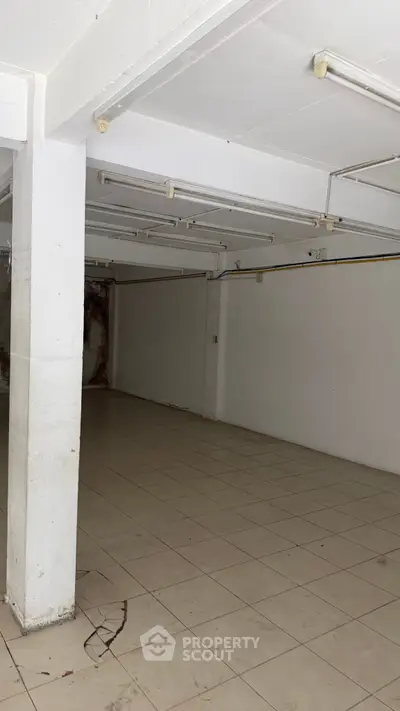 Spacious empty room with tiled flooring and exposed ceiling pipes, ideal for storage or renovation.