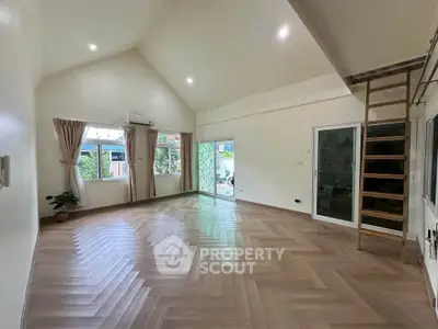 Spacious living room with high ceilings and wooden flooring, featuring large windows and a loft ladder.