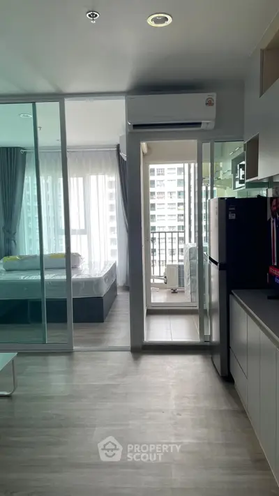 Modern apartment interior with bedroom, balcony, and kitchen area, featuring sleek design and natural light.