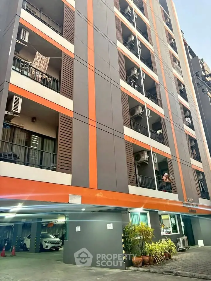 Modern multi-story apartment building with vibrant orange accents and parking area.