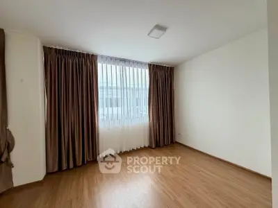 Spacious empty room with wooden flooring and large window with curtains