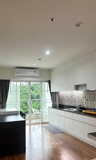 Modern kitchen with sleek cabinetry and balcony view, featuring open layout and natural light.
