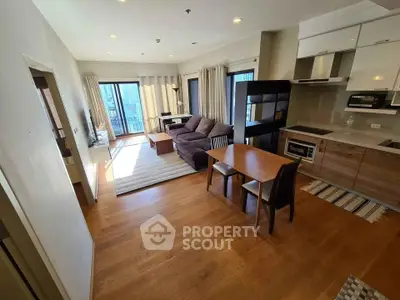 Modern living room with open kitchen and balcony view, featuring stylish furniture and wooden flooring.