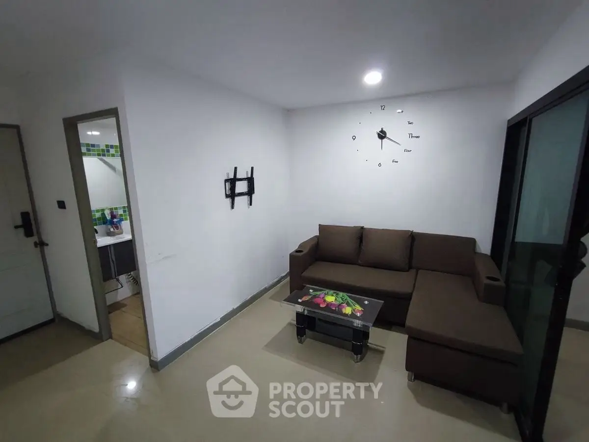 Modern living room with brown sectional sofa and wall clock, adjacent to a bathroom.