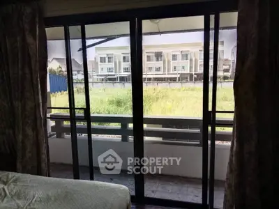 Spacious bedroom with sliding glass doors opening to a balcony with a view of modern townhouses.