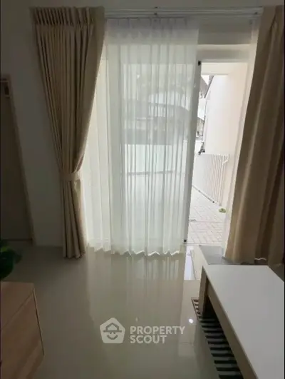 Bright living room with floor-to-ceiling windows and elegant curtains, offering a glimpse of the outdoor area.