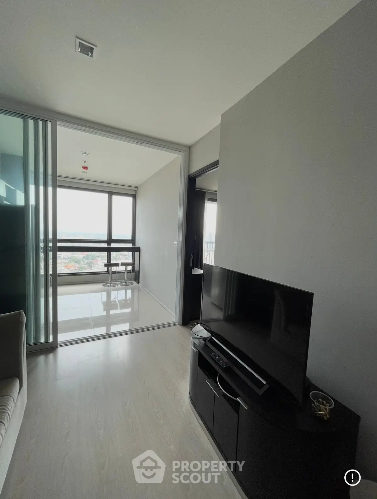Modern living room with sleek TV setup and glass sliding doors leading to a bright balcony with city views.