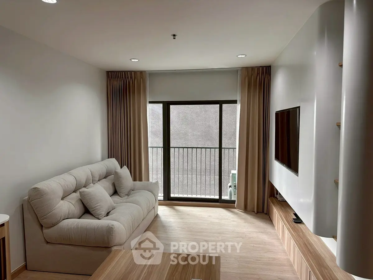 Modern living room with cozy sofa and wall-mounted TV, featuring elegant curtains and wooden flooring.