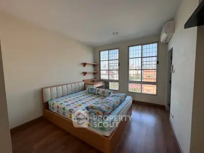 Cozy bedroom with wooden flooring and large windows offering city views