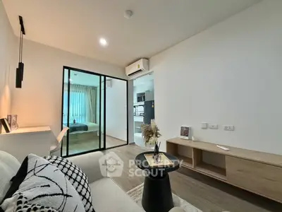 Modern living room with sliding glass doors leading to a cozy bedroom, featuring minimalist decor and natural light.