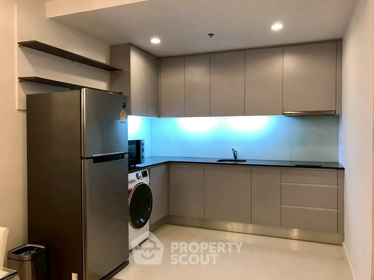 Modern kitchen with sleek cabinets, stainless steel fridge, and built-in washing machine.