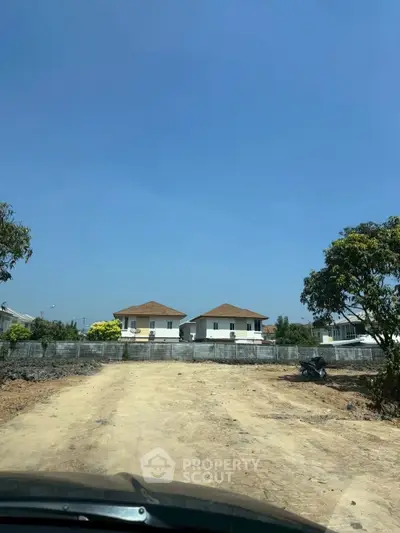 Spacious plot with clear blue sky and distant view of two modern houses, ideal for new development.