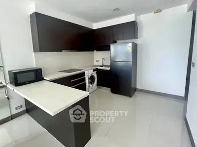 Modern kitchen with sleek dark cabinets, white countertops, and appliances including fridge and microwave.