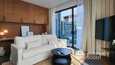 Modern living room with sleek sofa, large TV, and floor-to-ceiling windows opening to a private pool view.