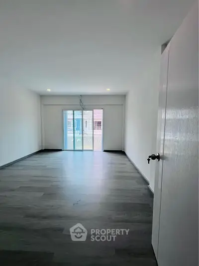 Spacious empty room with large window and modern flooring, perfect for customization.