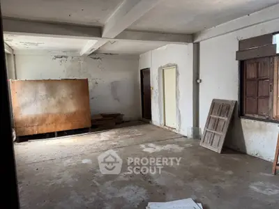 Spacious unfinished room with potential for renovation, featuring rustic wooden windows and concrete flooring.