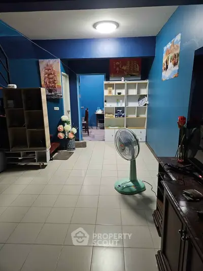 Spacious living room with blue walls and modern decor, featuring a fan and stylish shelving unit.