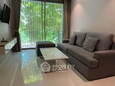 Modern living room with sleek gray sofa and large window offering lush green views.
