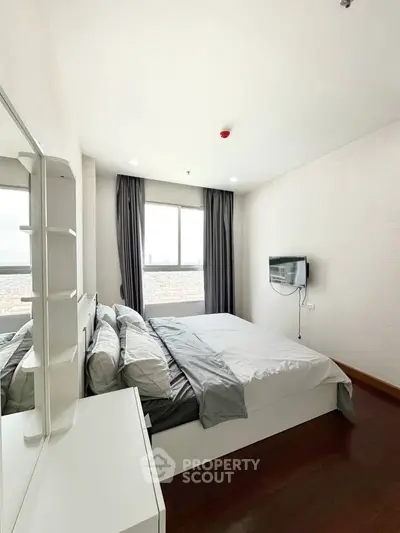Modern bedroom with large window and sleek furnishings in a high-rise apartment.