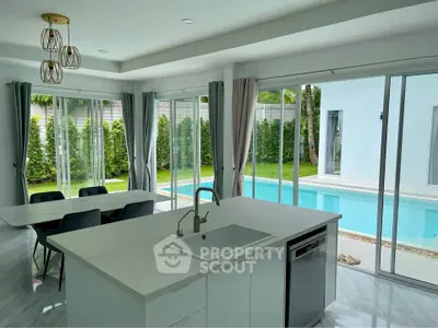 Luxurious open-plan kitchen with pool view, featuring modern island and dining area, perfect for entertaining.