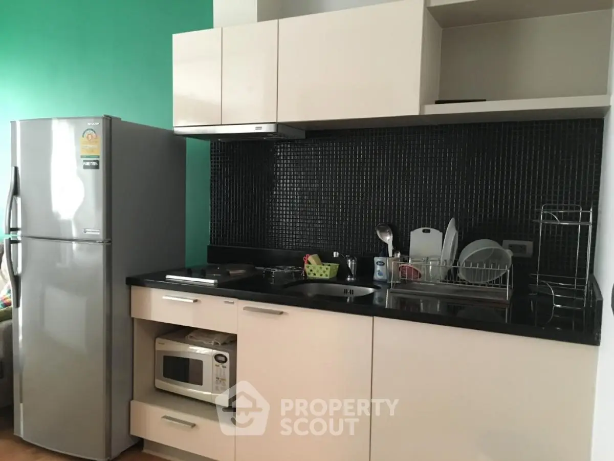 Modern kitchen with sleek cabinetry, stainless steel fridge, and microwave in a compact layout.