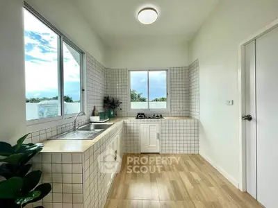 Bright and modern kitchen with large windows and gas stove, featuring sleek white tiles and wooden flooring.