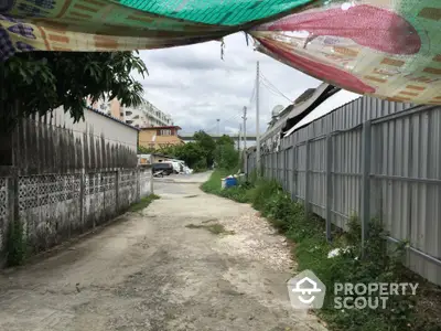 Narrow alleyway between residential buildings with overhanging tarp and cloudy sky.