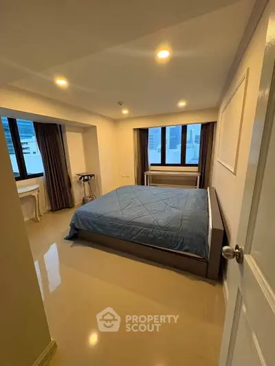 Spacious bedroom with large windows and modern furnishings in a high-rise apartment.