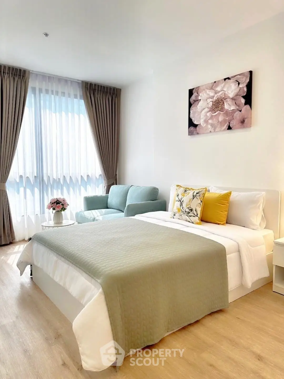 Bright and cozy bedroom with elegant decor and natural light, featuring a stylish sofa and floral artwork.