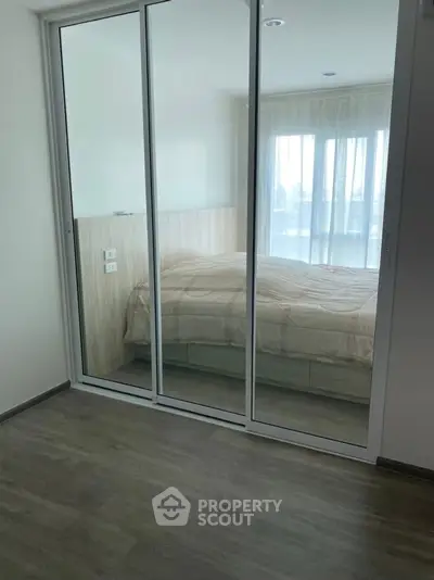 Modern bedroom with mirrored sliding closet doors and large window.