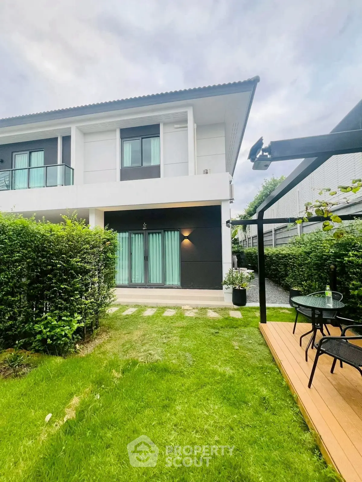 Modern two-story house with lush garden and patio seating area.