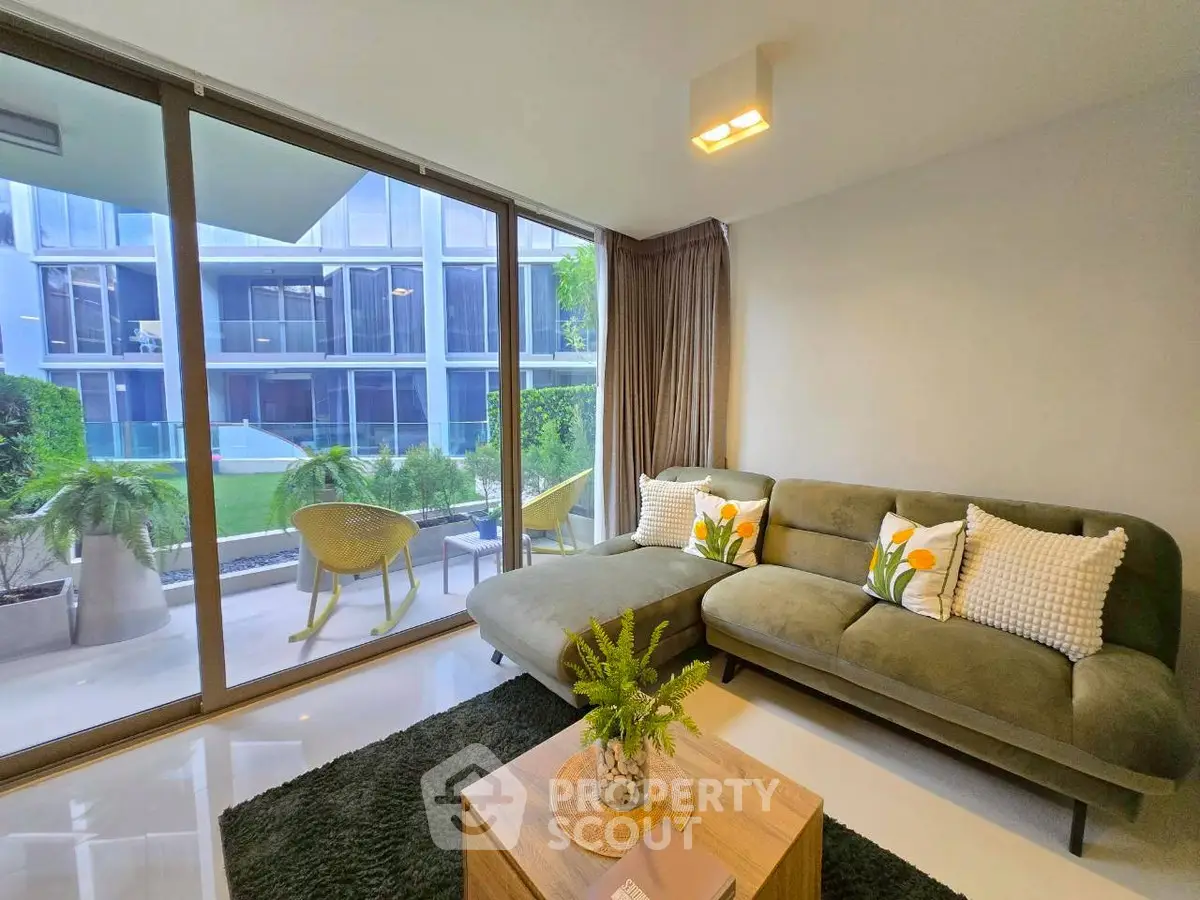 Modern living room with large windows and stylish green sofa, overlooking a serene garden view.