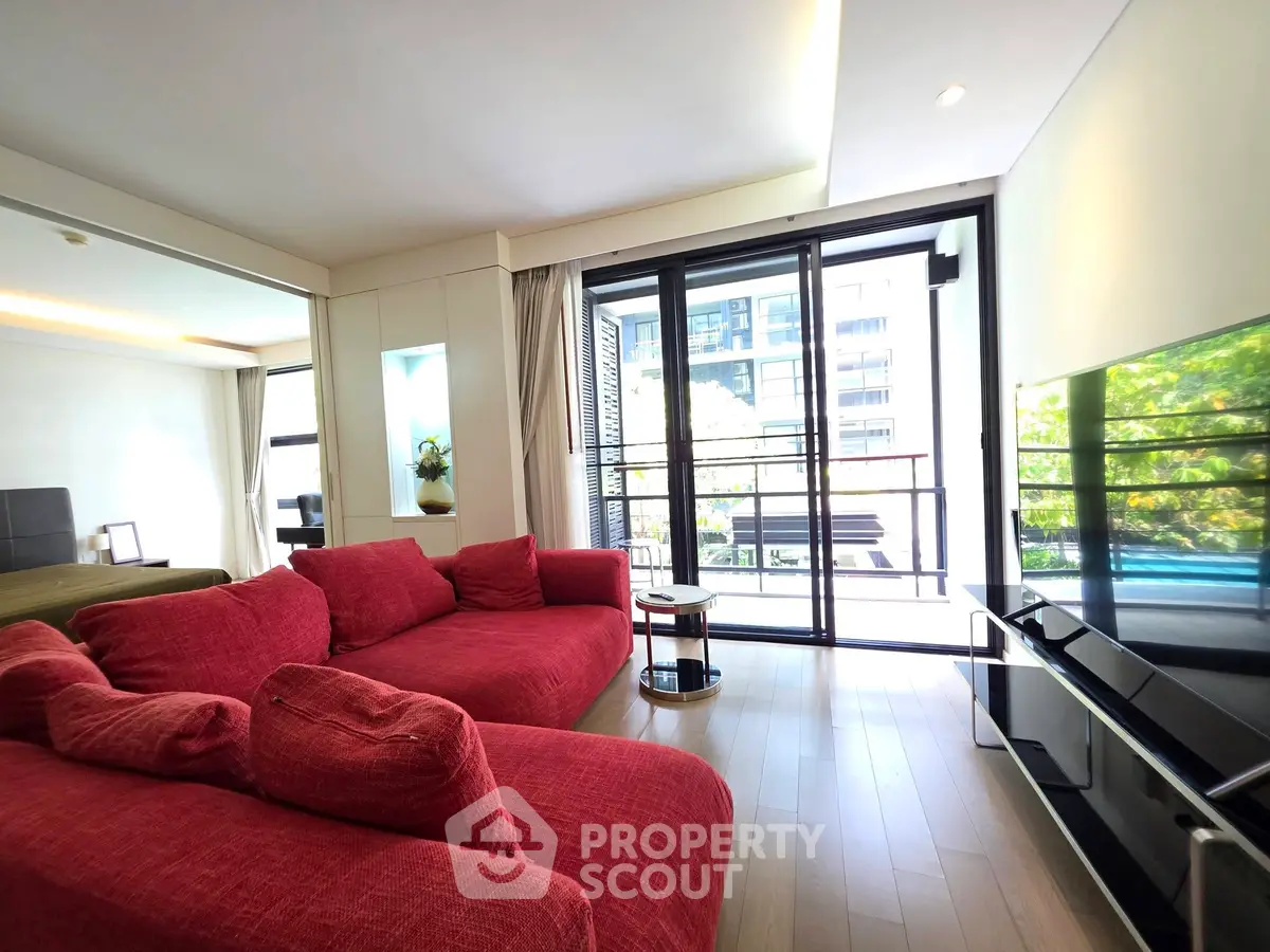 Spacious living room with vibrant red sofas and large windows offering natural light and a view of greenery.
