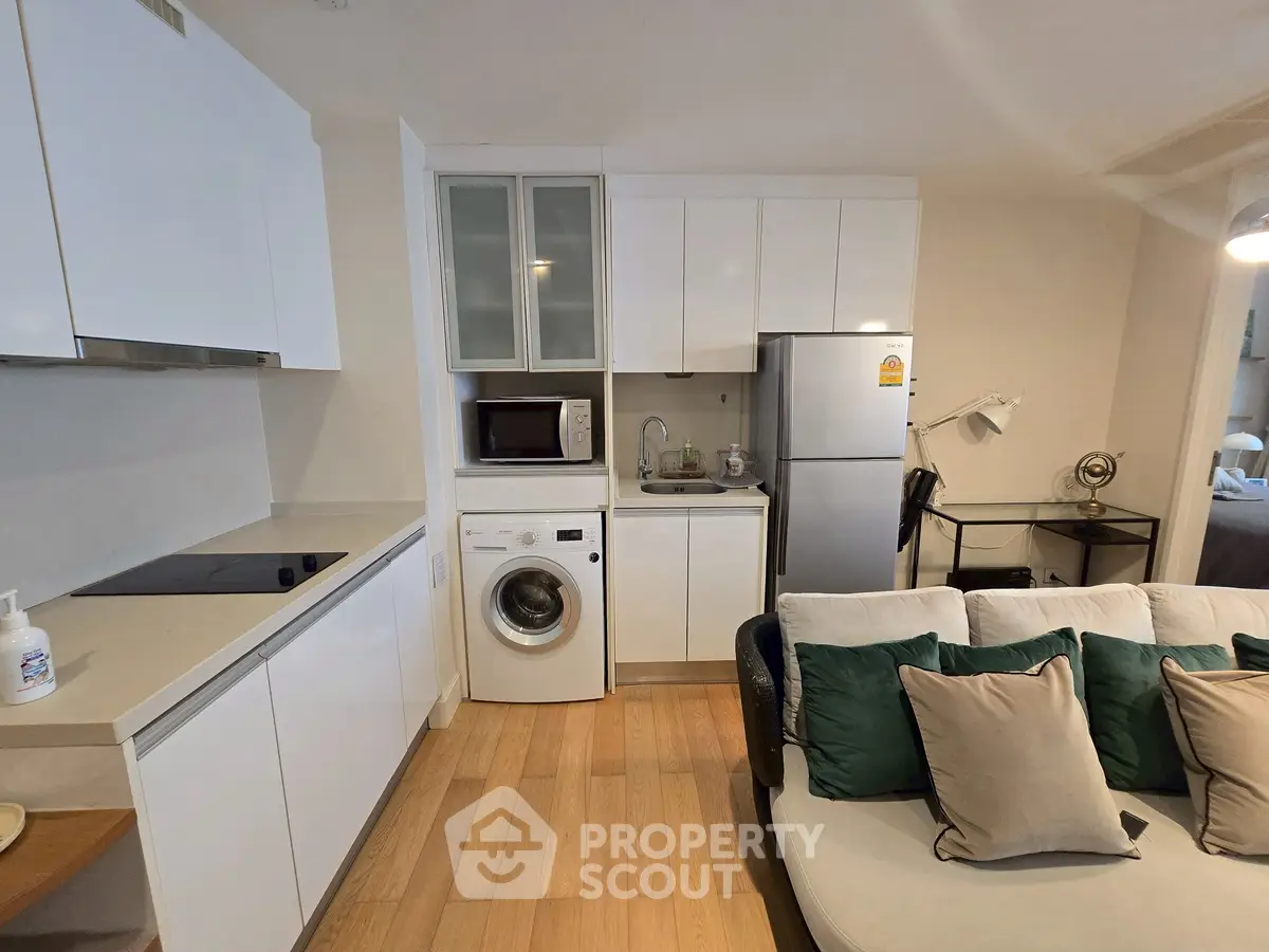 Modern kitchen with sleek white cabinets, washing machine, and cozy living area with stylish sofa.