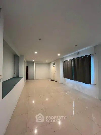 Spacious empty living room with tiled flooring and large windows.