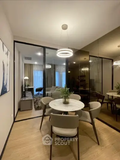 Modern dining area with elegant lighting and glass partition leading to cozy living room.