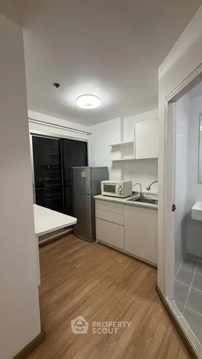 Modern kitchen with sleek white cabinets, stainless steel fridge, and wooden flooring in a contemporary apartment.