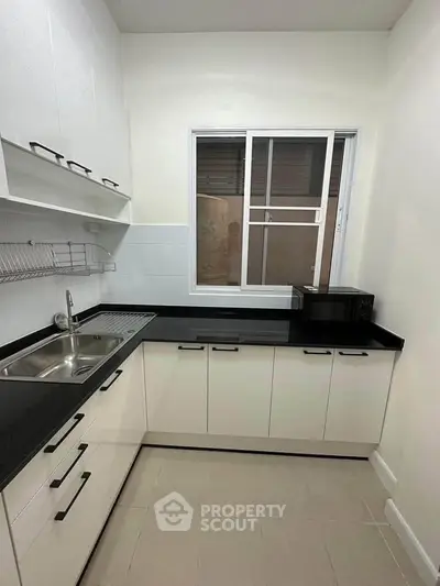 Modern kitchen with sleek white cabinets and black countertops, featuring a compact design and ample storage space.