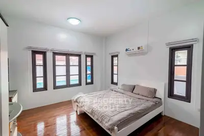 Spacious bedroom with wooden flooring and large windows offering natural light.
