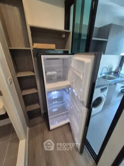 Modern kitchen with open fridge and washing machine, sleek cabinetry, and wood flooring.