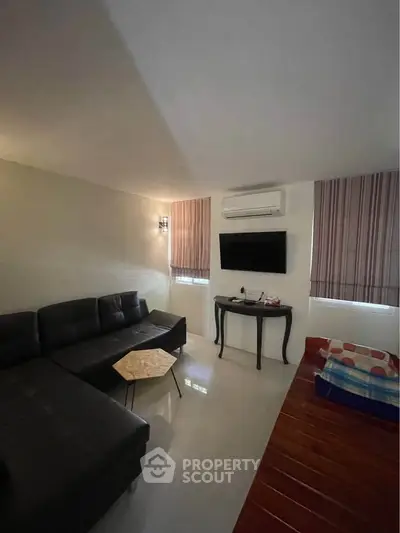 Cozy living room with modern black sofa, wall-mounted TV, and air conditioning.