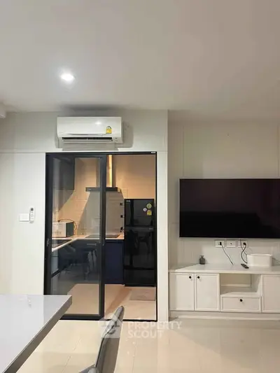 Modern living room with open kitchen and sleek appliances, featuring a wall-mounted TV and air conditioning.