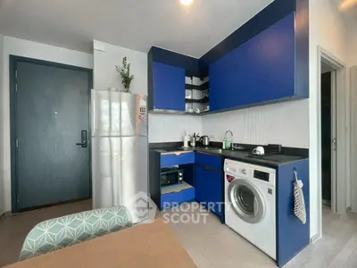 Modern kitchen with blue cabinets, washing machine, and stainless steel fridge in a stylish apartment.