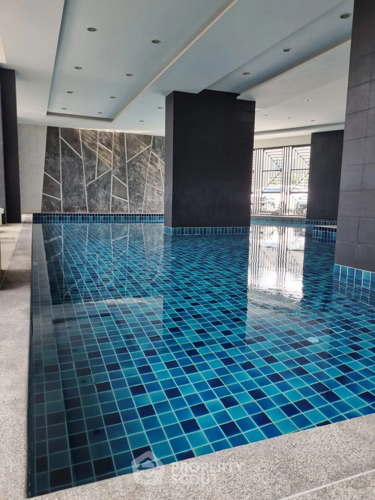 Luxurious indoor pool with modern design and blue mosaic tiles in upscale residential building.