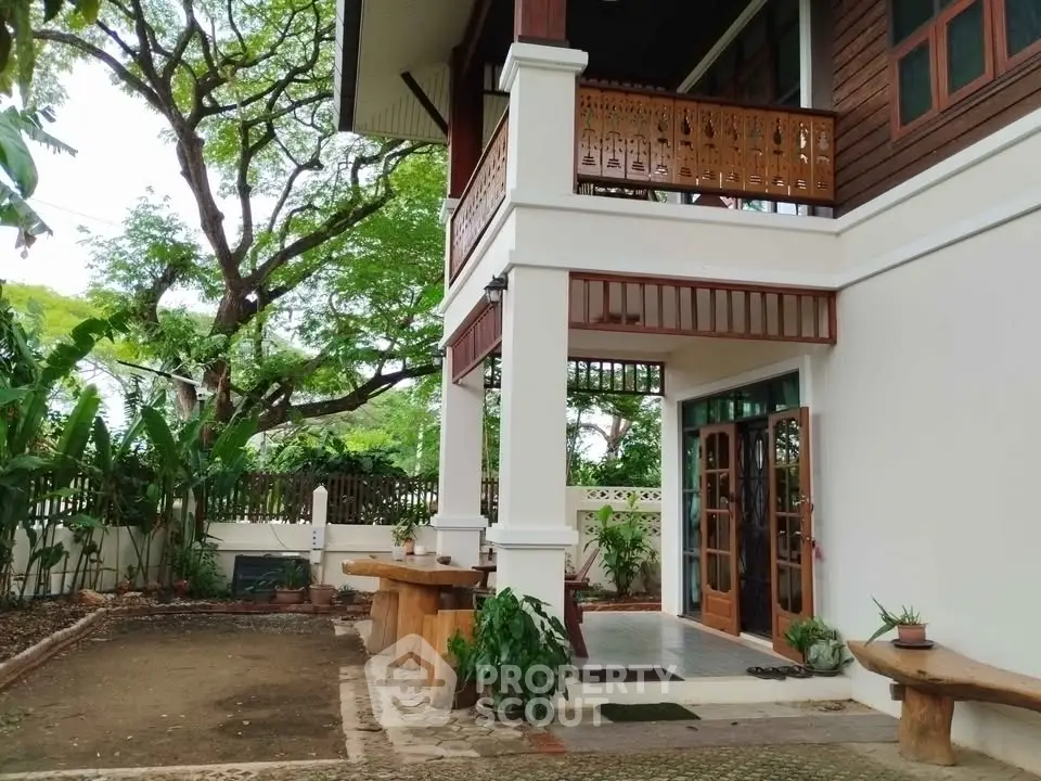 Charming two-story home with wooden balcony and lush garden setting.