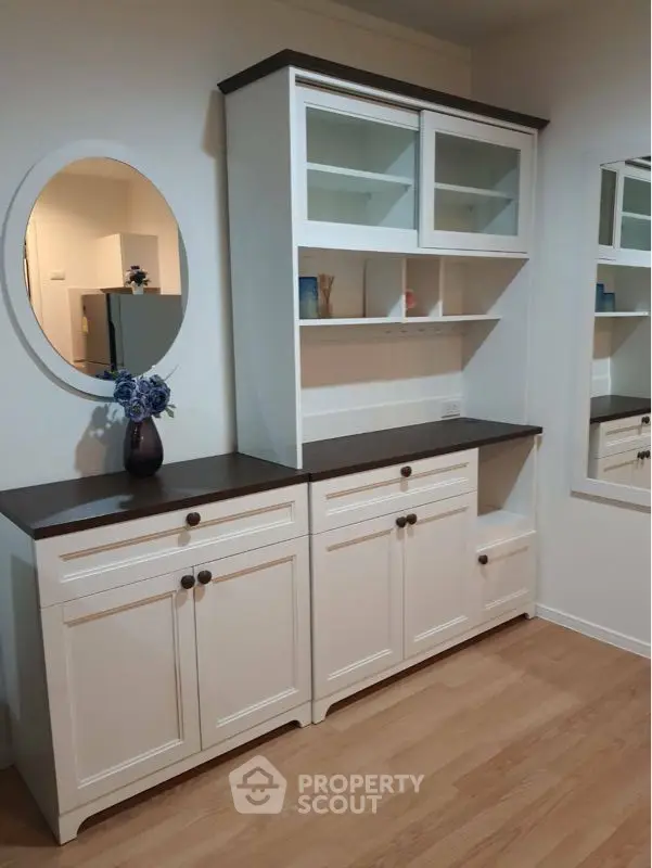 Elegant built-in white cabinetry with contrasting dark countertop and stylish round mirror, perfect for a refined living space with ample storage.