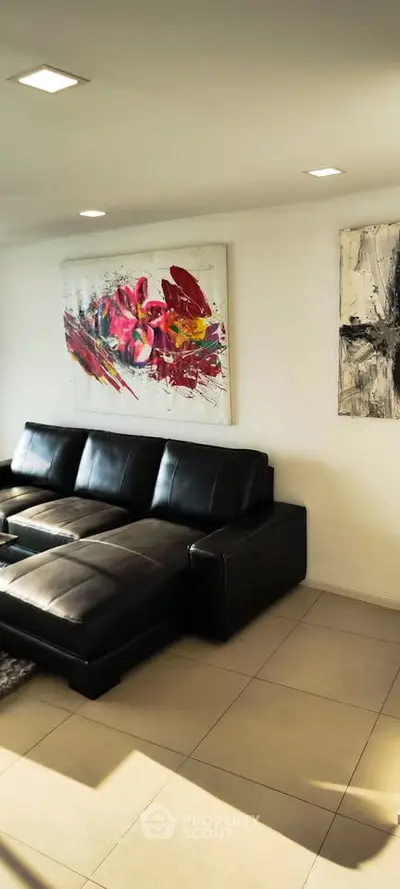 Modern living room with black leather sofa and vibrant abstract art on white walls.